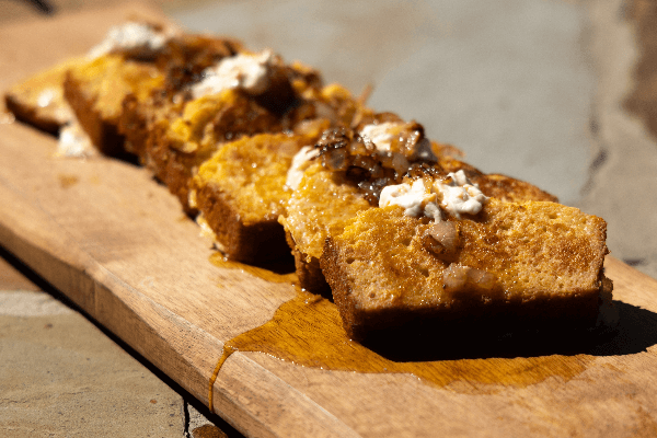 knotts cornbread and pimiento cheese french toast stacked on a wooden board with syrup and bacon topping