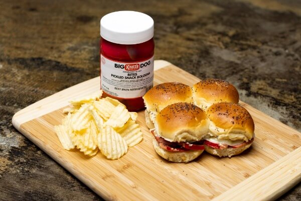 fried pickled bologna sliders on a wooden board with chips and a container of knotts big dog bites of pickled snack bologna