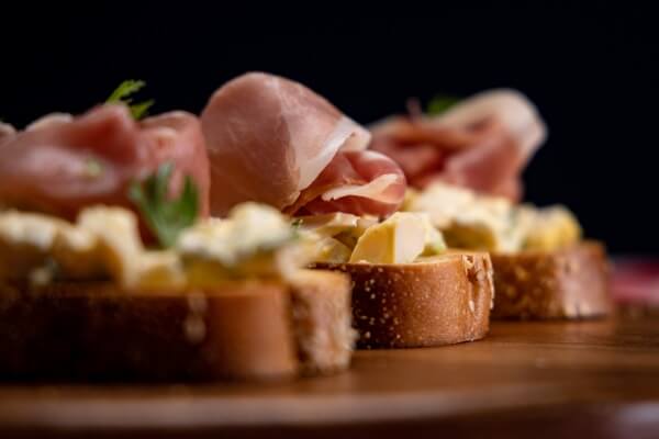 pickled egg toasts with herbs and prosciutto on a wooden board