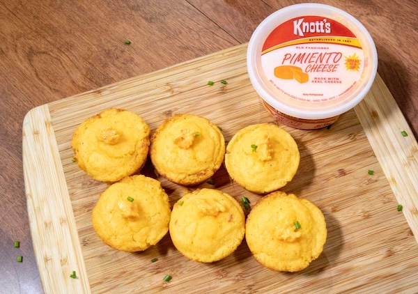 pimiento cheese cornbread muffins on a wooden board with a container of knott's pimiento cheese