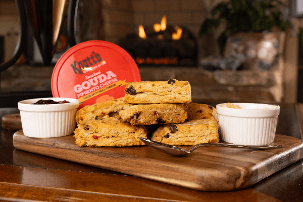 smoked gouda and apricot scones stacked on a board with jars of jam and spread with container of smoked gouda pimiento cheese and fireplace in the background