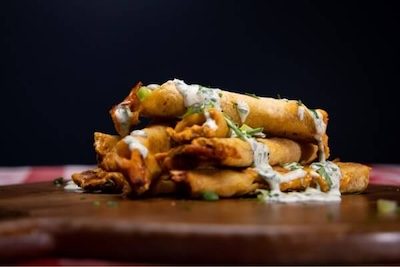 spicy chicken taco tajuitos stacked on a board with creme fresh drizzle over top