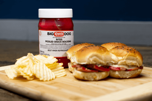 pickled snack bologna slider with jar of pickled snack bologna and chips on a wooded board